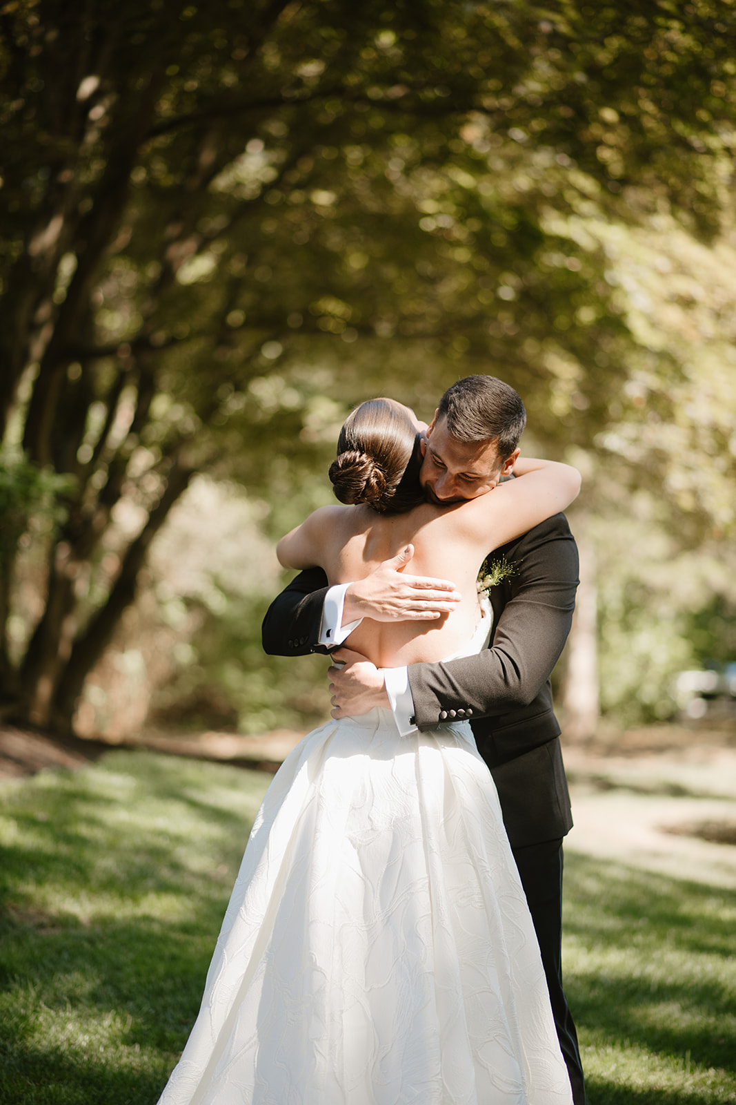 Groom hugging the bride tightly while smiling with closed eyes during their first look outdoors.